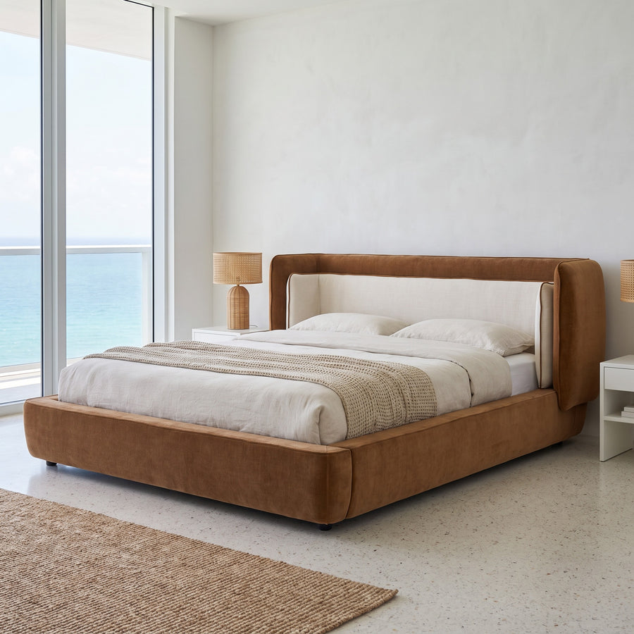 Cognac and off-white wingback bed in a bright waterfront condo bedroom, floor-to-ceiling ocean-view window, midday coastal light.
